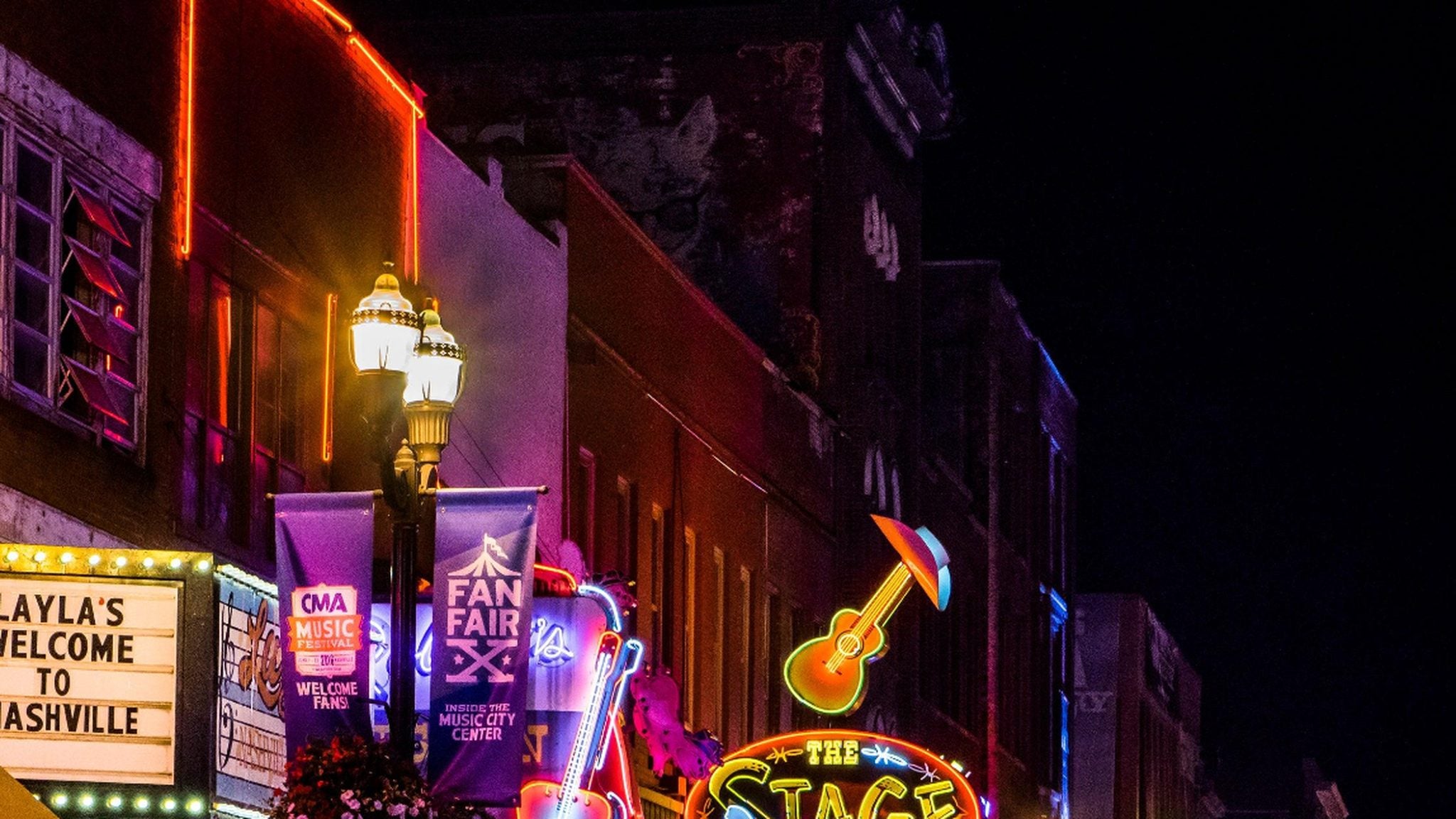 A Nashville-style nightlife strip lit with colorful neon signs, reflected on the wet street