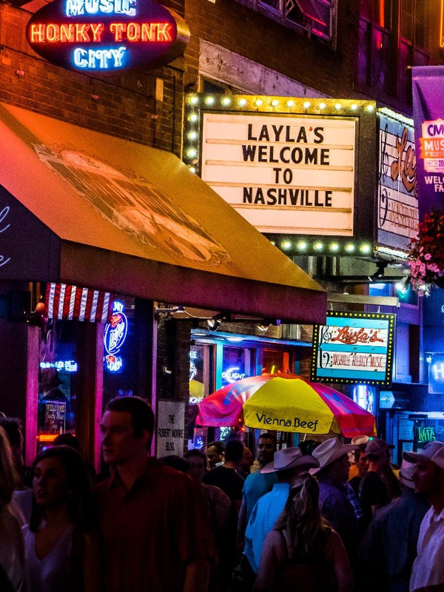 A Nashville nightlife street with neon signs and a crowd outside the bars