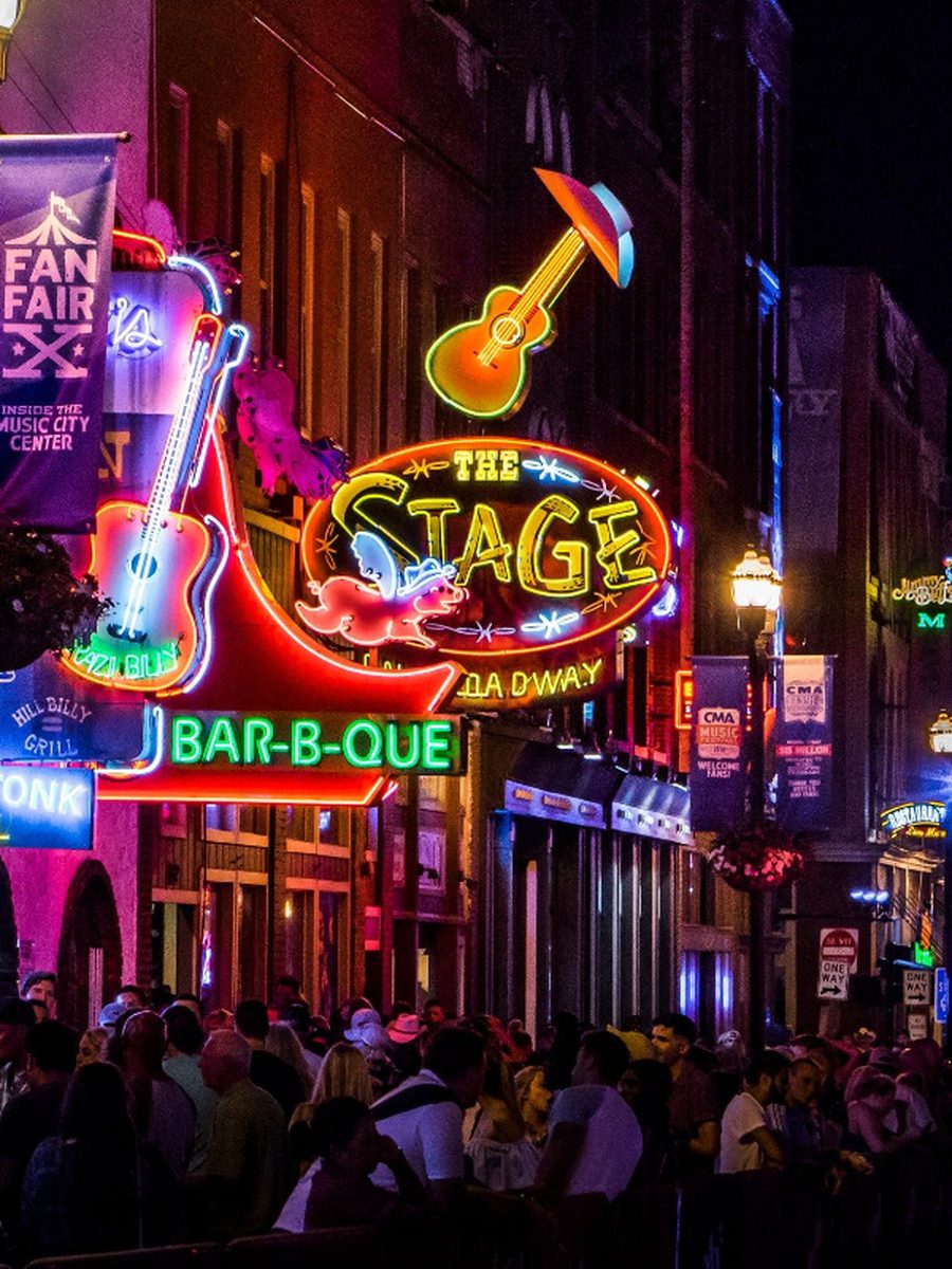 Neon guitar and barbecue signs glowing above a busy Nashville sidewalk